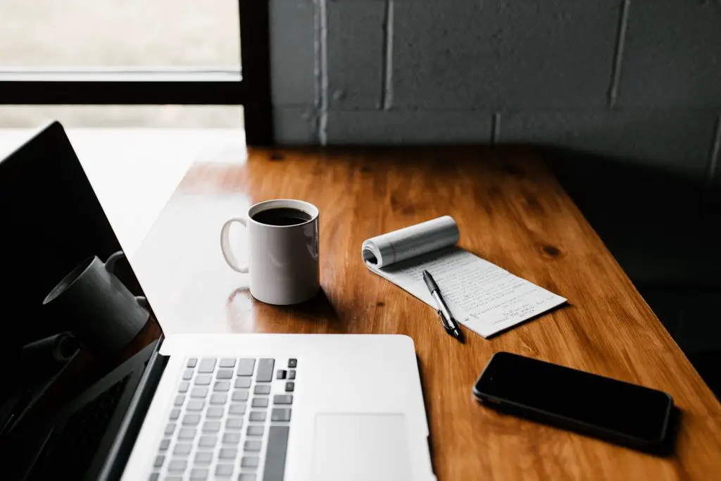 laptop with coffee, phone and checklist paper on a table